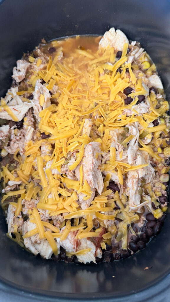 cooked chicken, corn, beans, tomatoes, and seasoning topped with shredded cheese in base of crockpot