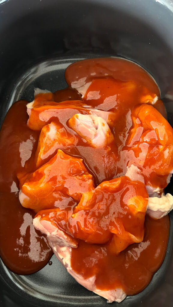 Chicken breasts in a slow cooker bowl with red enchilada sauce.