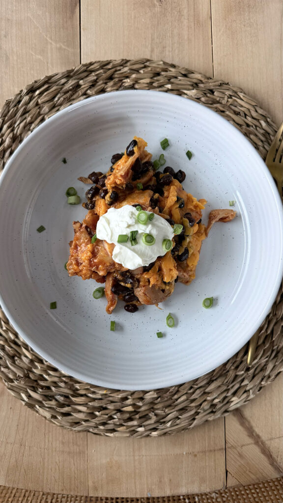 Overhead image of slow cooker chicken enchilada casserole with a dollop of sour cream on top.