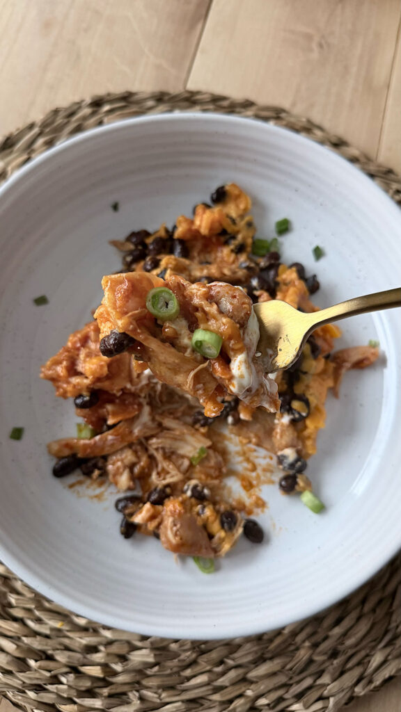 A gold fork holding up a bite of slow cooker chicken enchilada casserole on a white plate.
