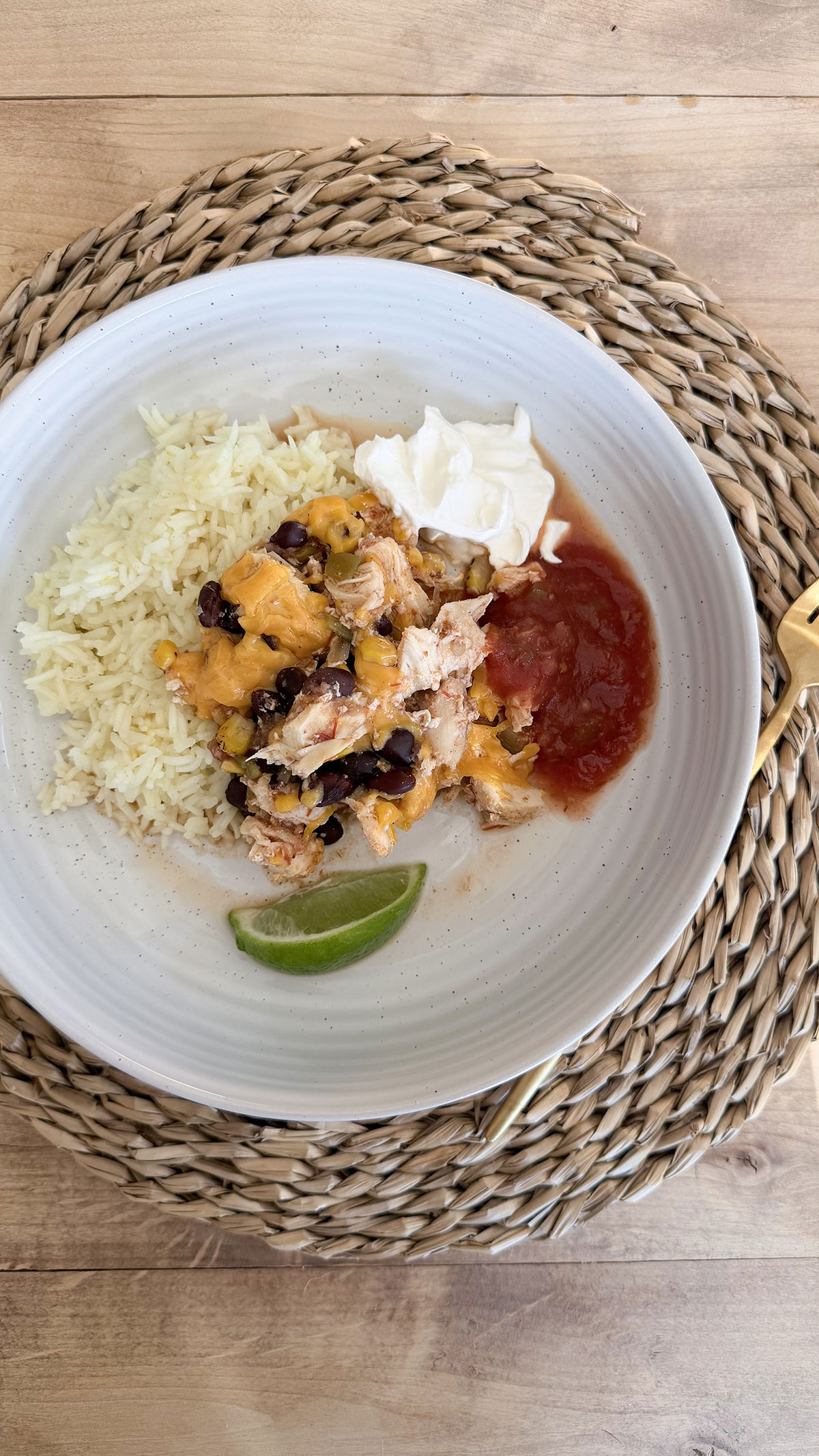crockpot chicken burrito bowl filling surrounded by rice, sour cream, salsa, and a lime wedge plated in white bowl on placemat