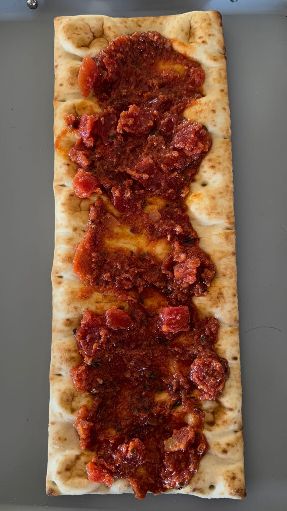 flatbread pizza crust topped with bruschetta sauce, on baking sheet