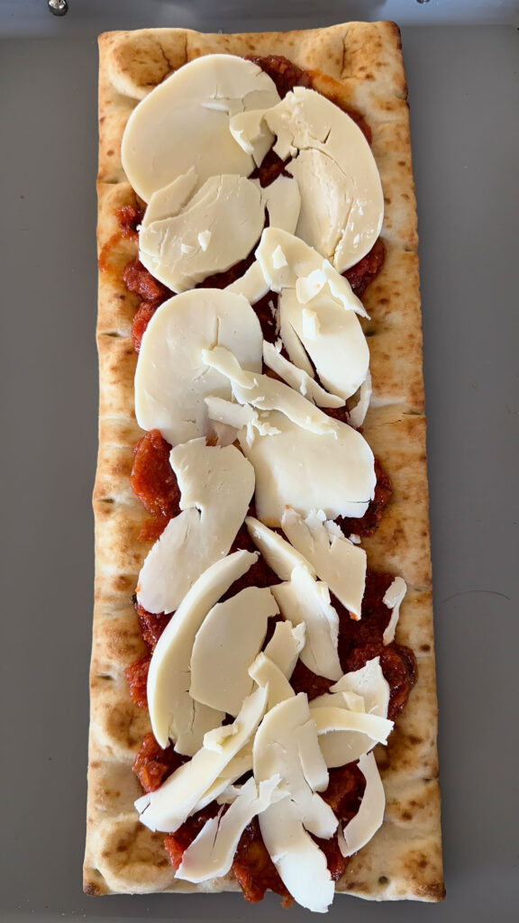 flatbread pizza crust topped with bruschetta sauce and sliced mozzarella, on baking sheet
