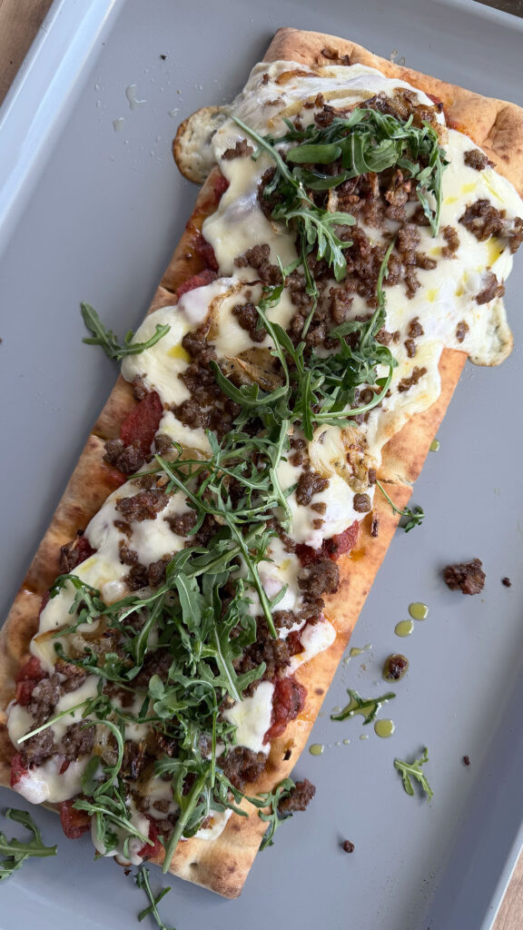 Cooked caramelized onion and sausage pizza with mozzarella cheese and arugula on a baking sheet