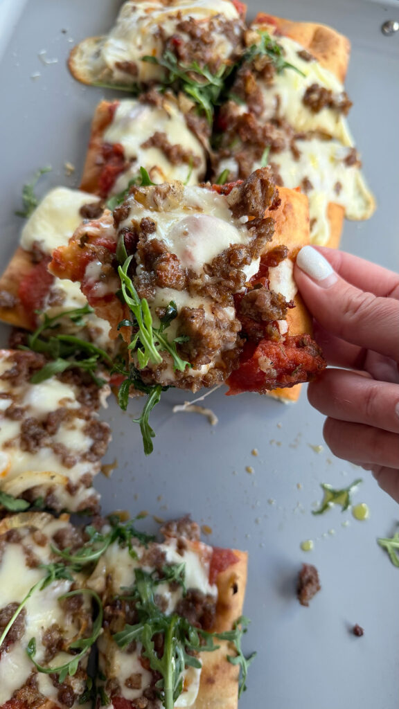 hand hold a slice of caramelized onion and sausage pizza with the rest of the pizza in the background on a baking sheet