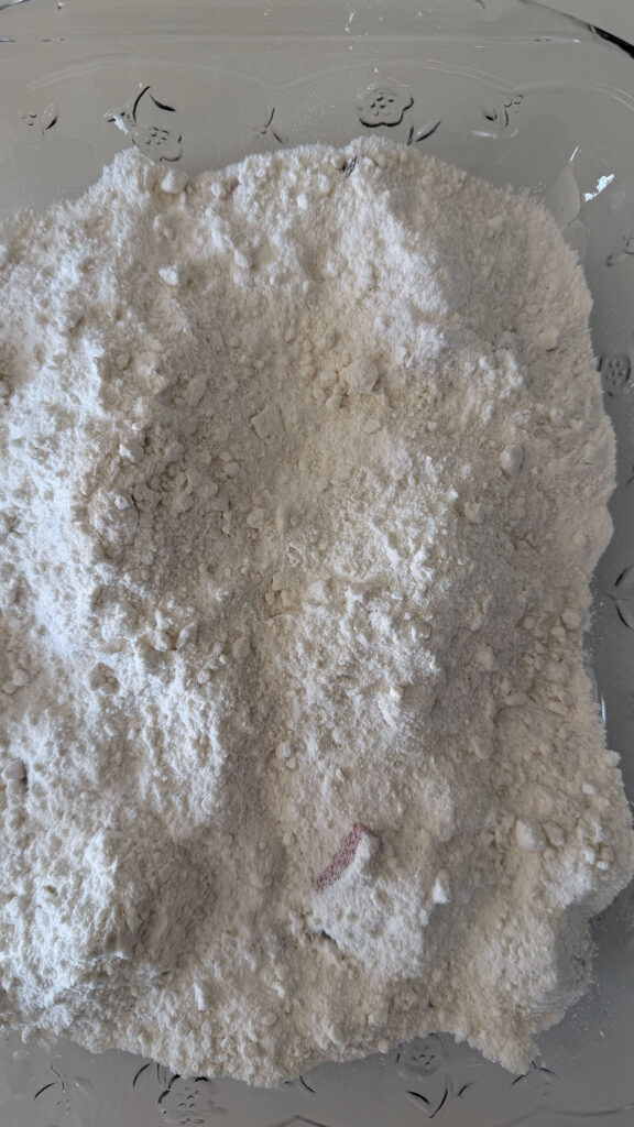 Unbaked boxed cake mix covering sliced strawberries and strawberry jell-o powder in clear baking dish