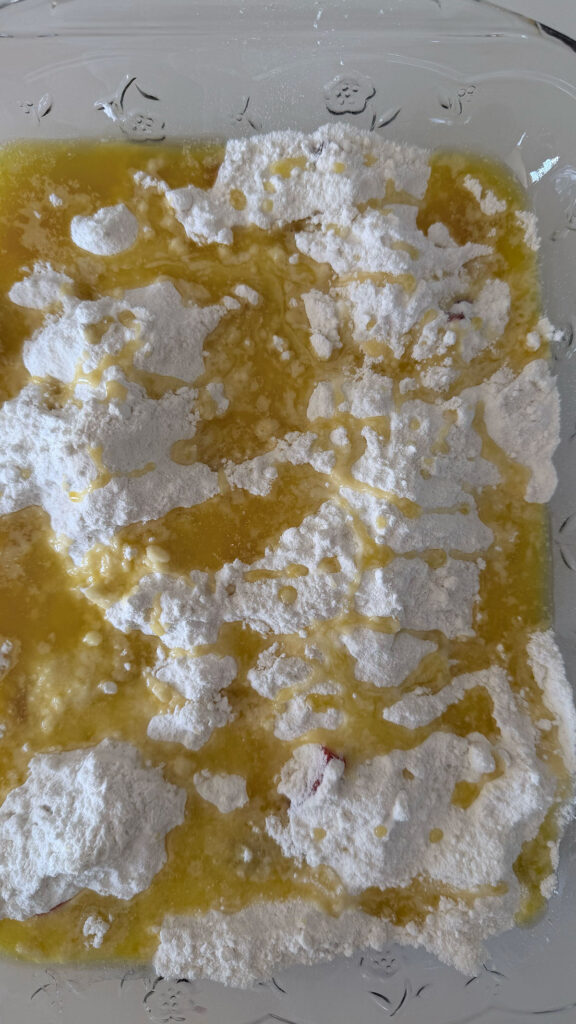 Melted butter drizzled on top of unbaked boxed cake mix covering sliced strawberries and strawberry jell-o powder in clear baking dish