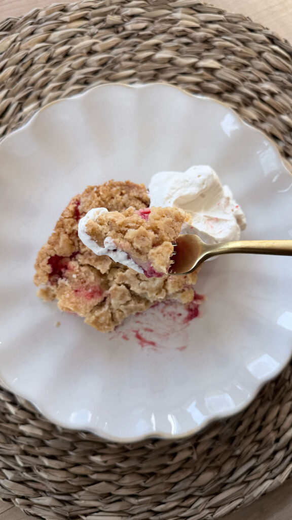 Spoonful of strawberry dump cake with slice of strawberry dump cake on white plate with dollop of whipped cream in background. Placemat behind white plate.