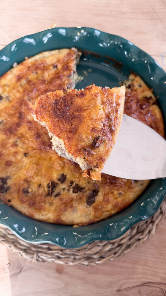 Slice of baked cheeseburger pie on spatula. Rest of cheeseburger pie in teal pie plate on placemat in background.