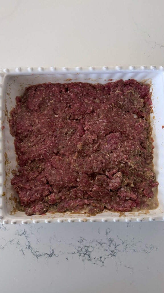 raw ground meat in bottom of white baking dish