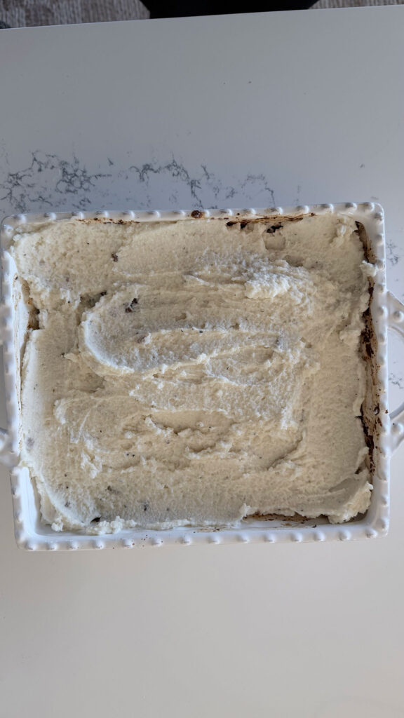 raw meat in bottom of white baking dish topped with mashed potatoes