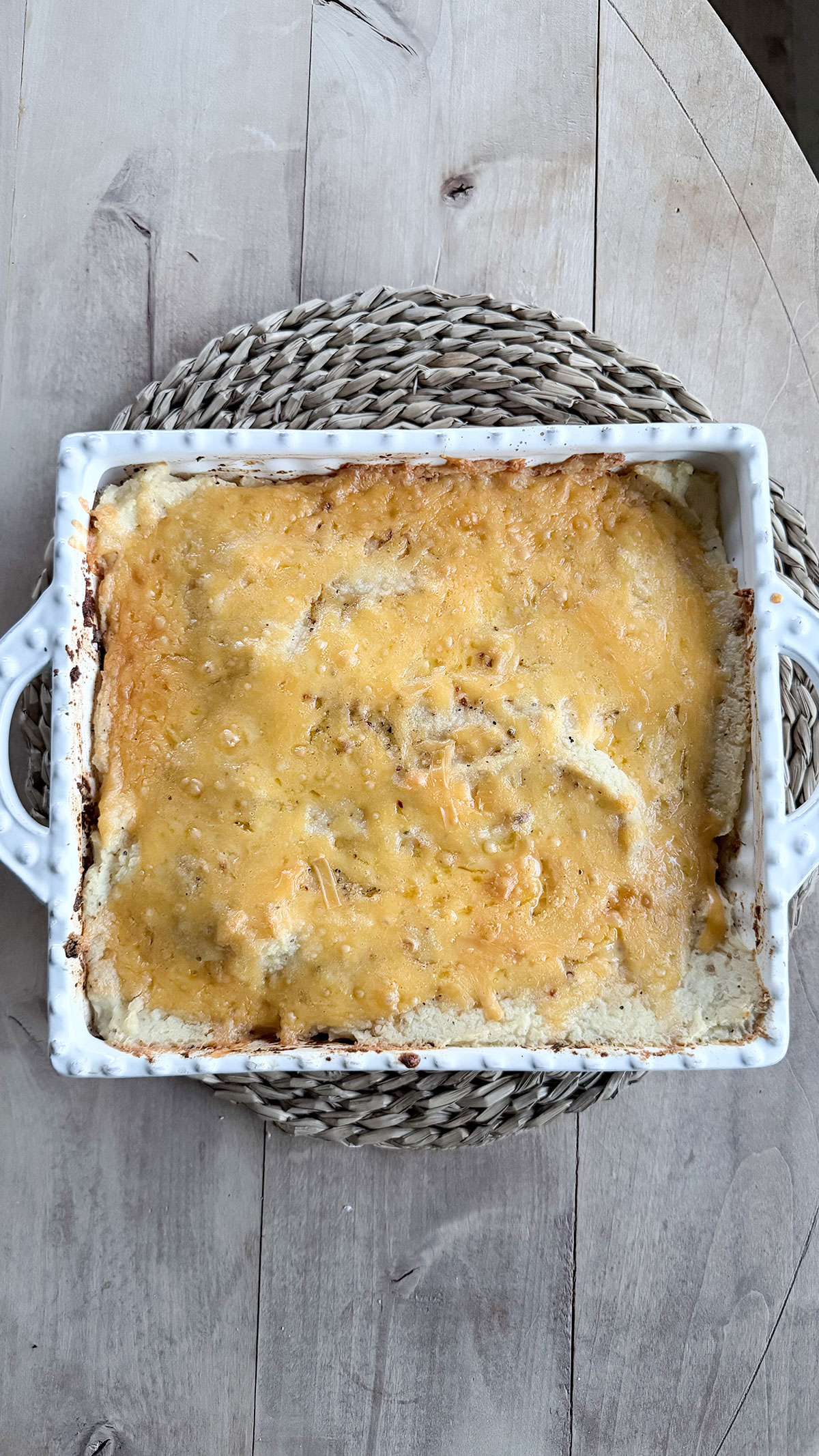 cooked meatloaf casserole in white dish on top of placemat on wood table