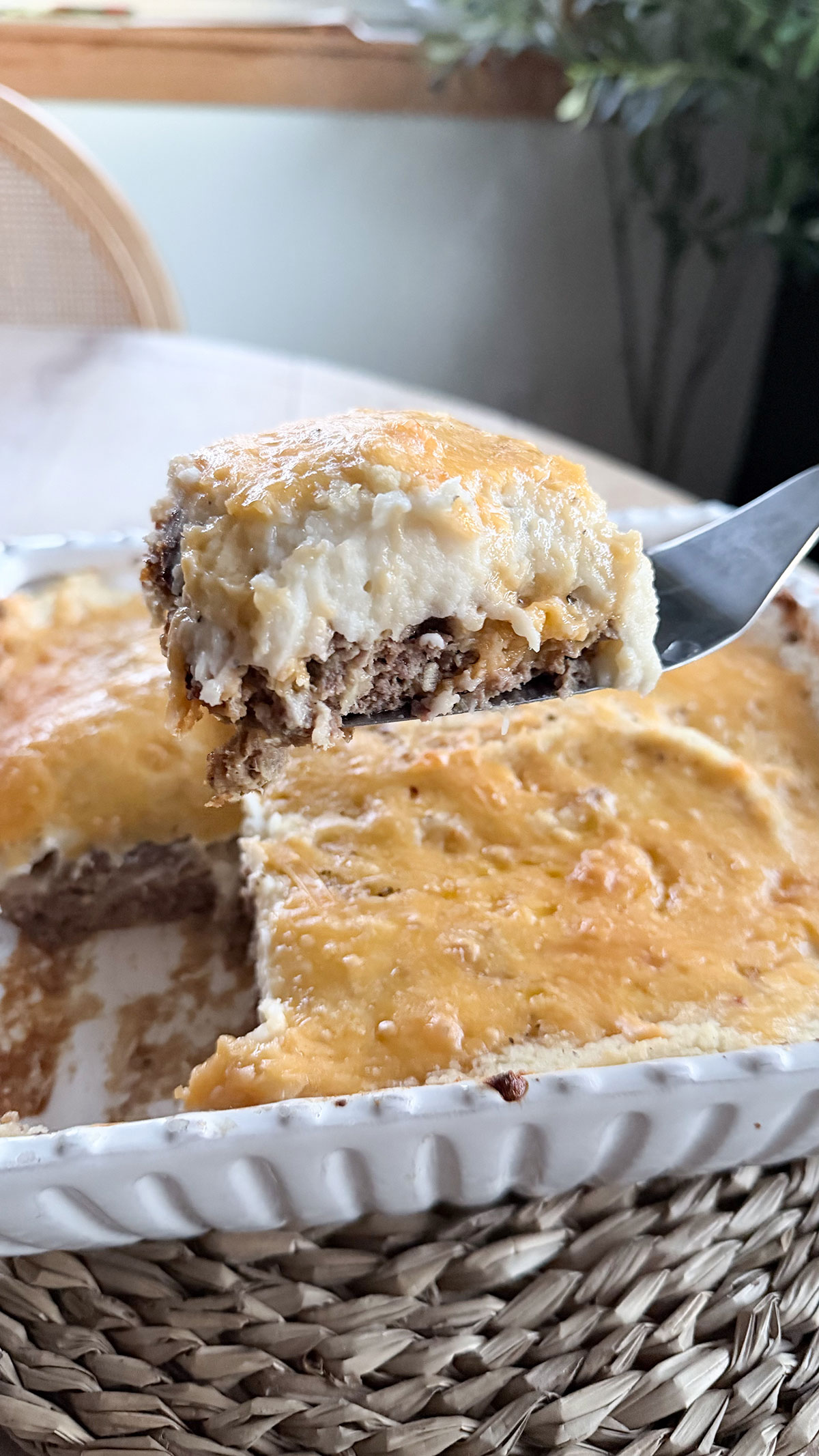 slice of cooked meatloaf casserole on spatula coming out of dish with table and chair in background