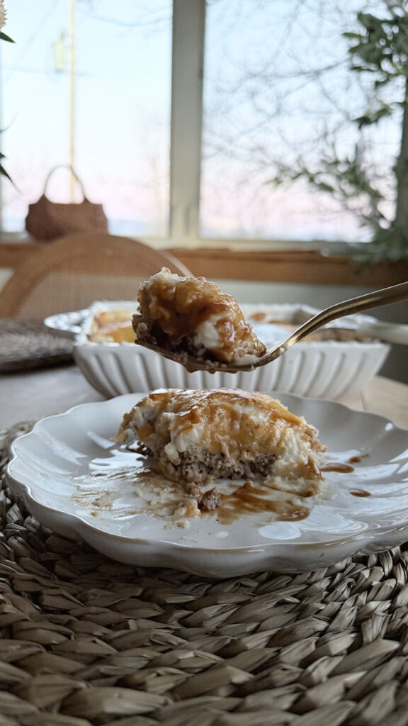 Forkful of cooked meatloaf casserole with individual serving on plate, and casserole dish, in background