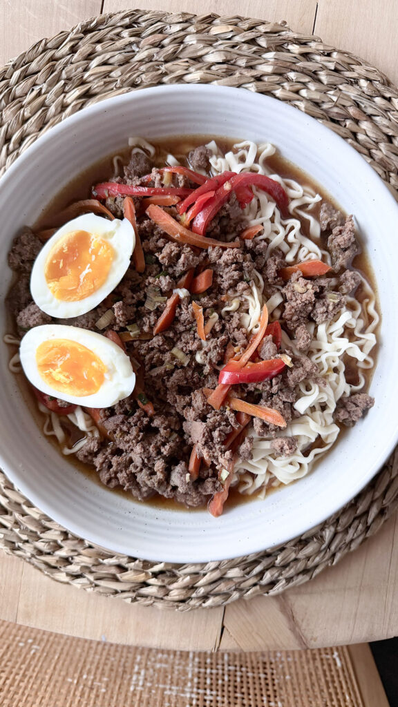 A white bowl with slow cooker beef ramen on a wicker placemat.