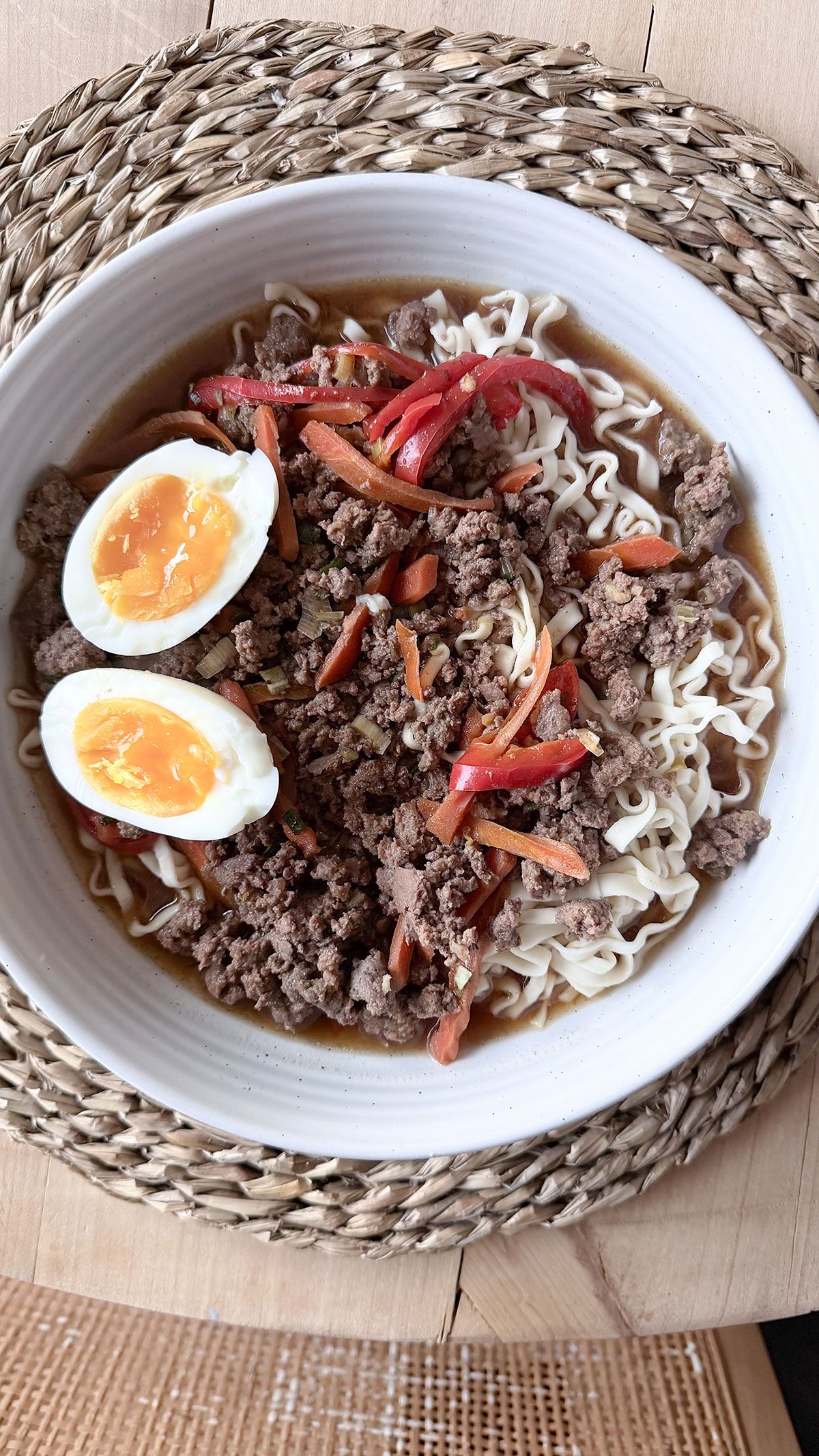 A white bowl with slow cooker beef ramen on a wicker placemat.