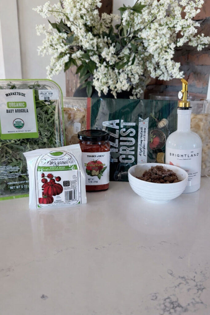 ingredients for caramelized onion and sausage pizza on white countertop with flowers in background