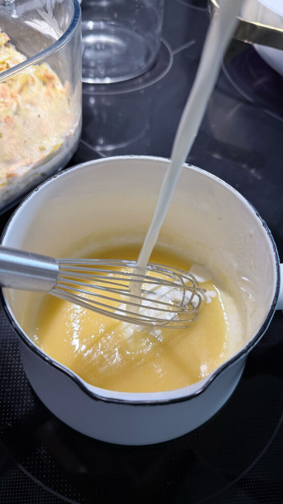 milk being poured into flour butter mixture, with whisk