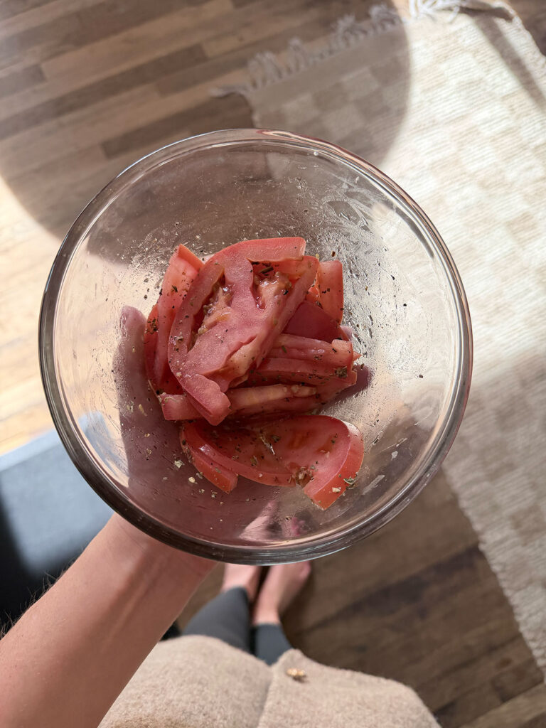 sliced tomatoes with dressing and seasoning in clear glass bowl