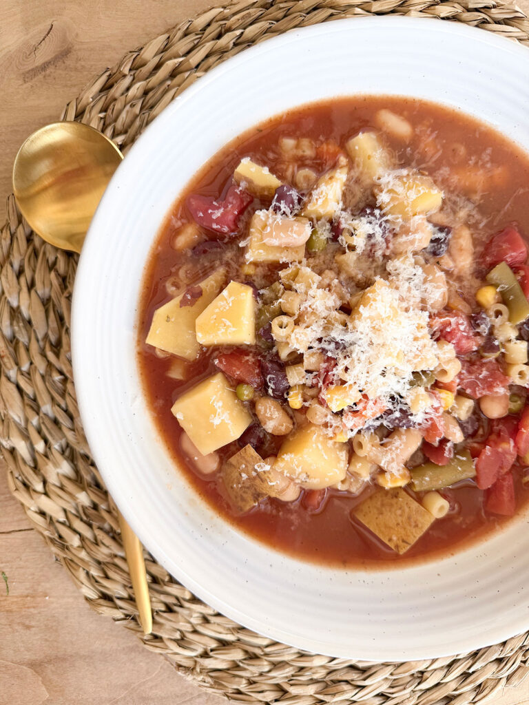 bowl of crockpot minestrone in white bowl on placemat with gold spoon