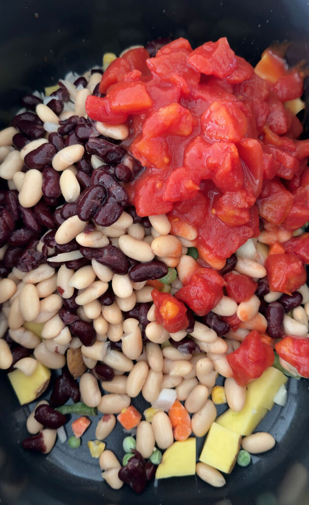 beans and canned tomatoes added to crockpot with veggies in it