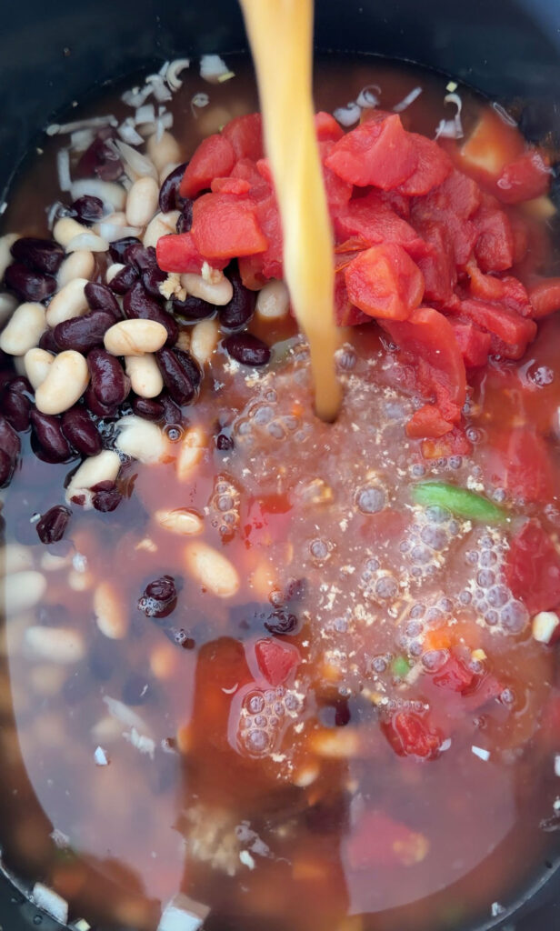 broth being added to crockpot with v8, canned tomatoes, beans and veggies