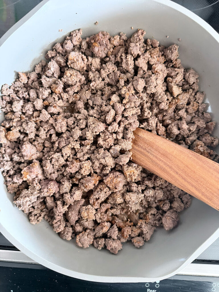 browning ground beef in pan with wooden spoon