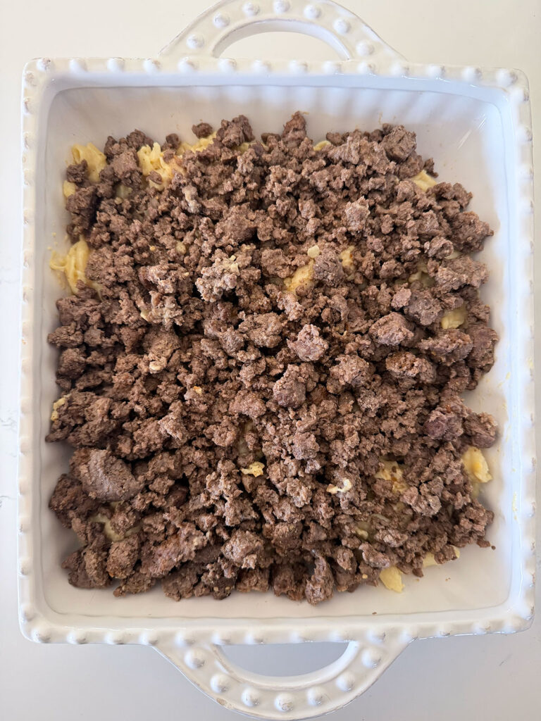 mac and cheese taco bake in white baking dish, uncooked, with layer of ground beef