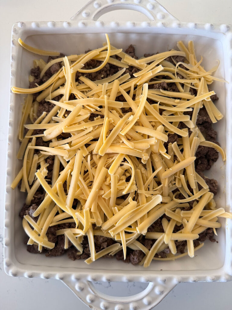 mac and cheese taco bake in white baking dish, uncooked, topped with cheddar cheese
