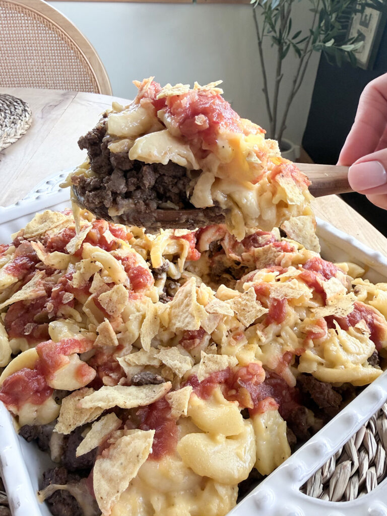 mac and cheese taco bake in white baking dish with hand holding wooden spoon