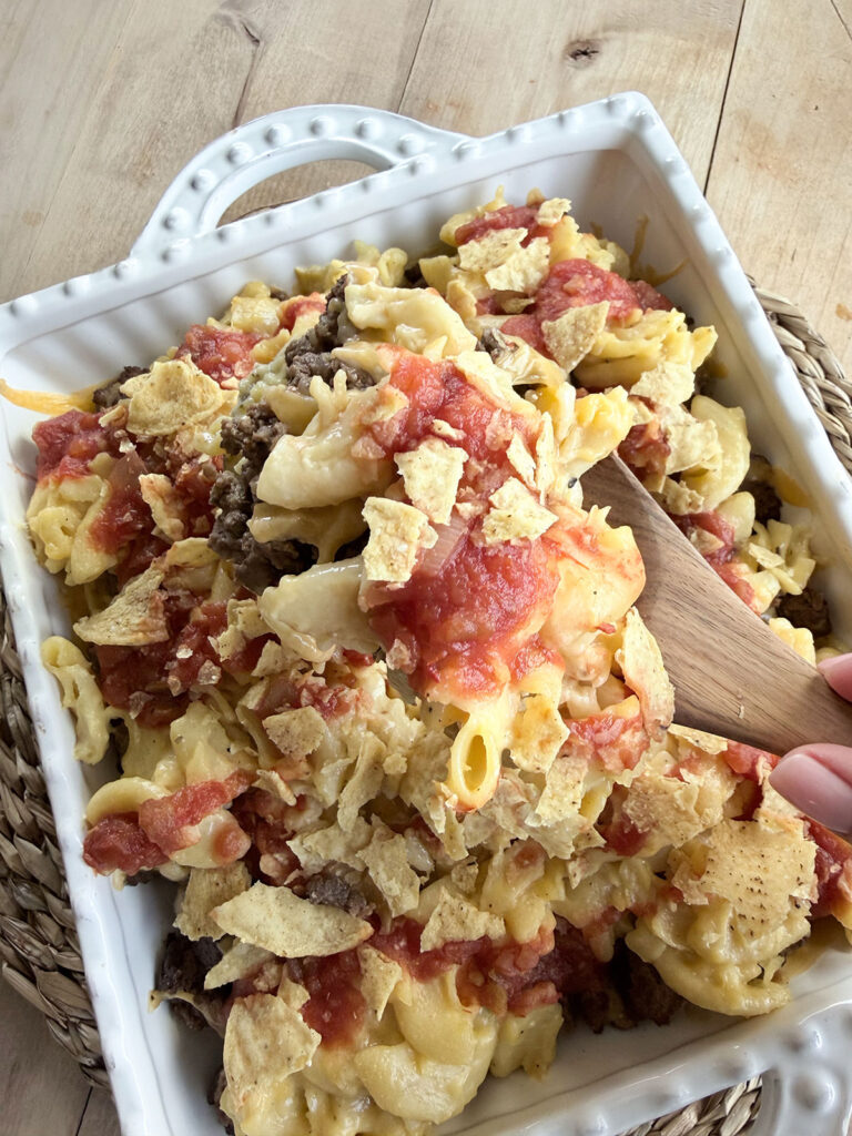 mac and cheese taco bake in white baking dish with wooden spoon