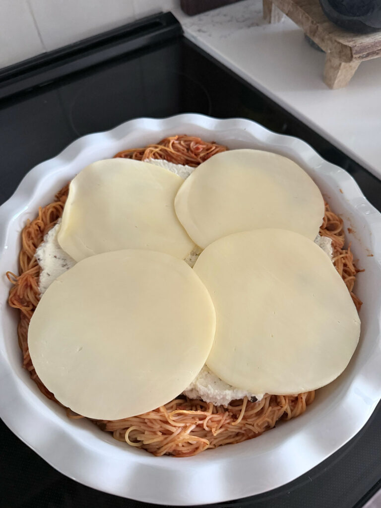 spaghetti pie topped with cheese, unbaked