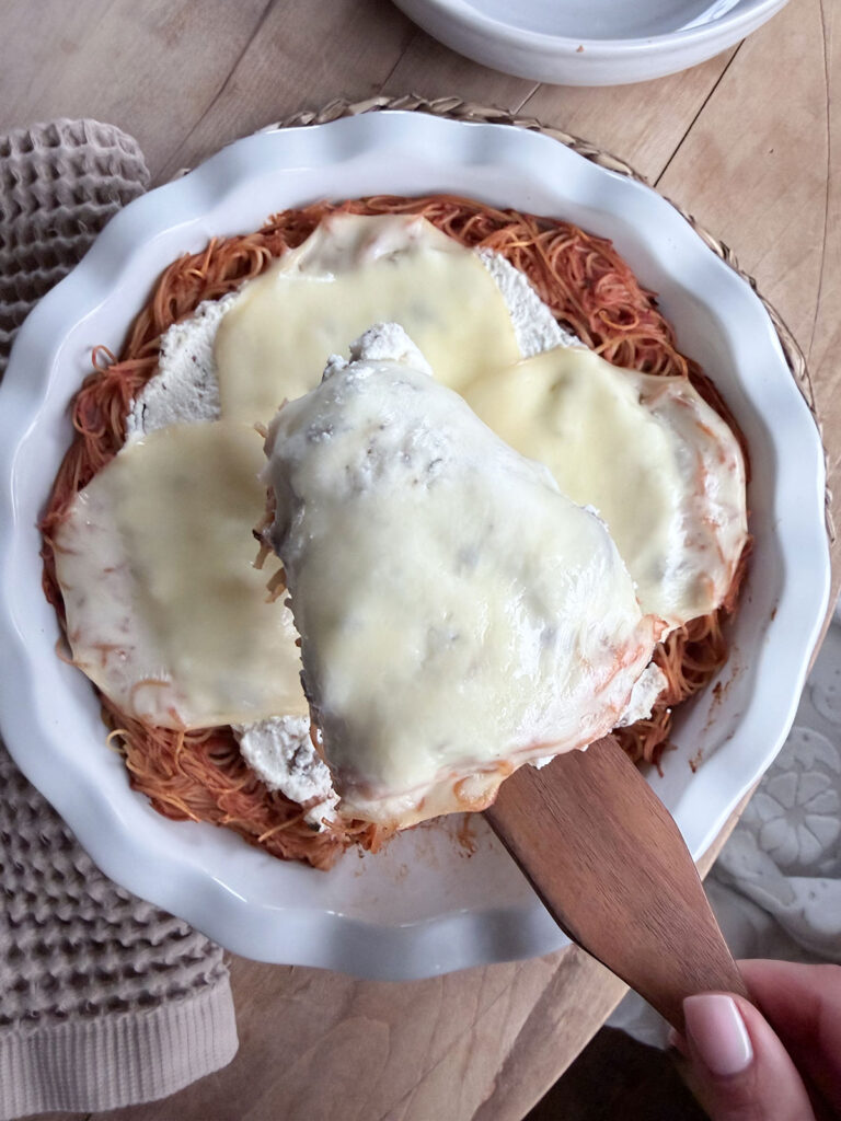 slice of spaghetti pie removed with wooden spatula. spaghetti pie in dish beneath it.