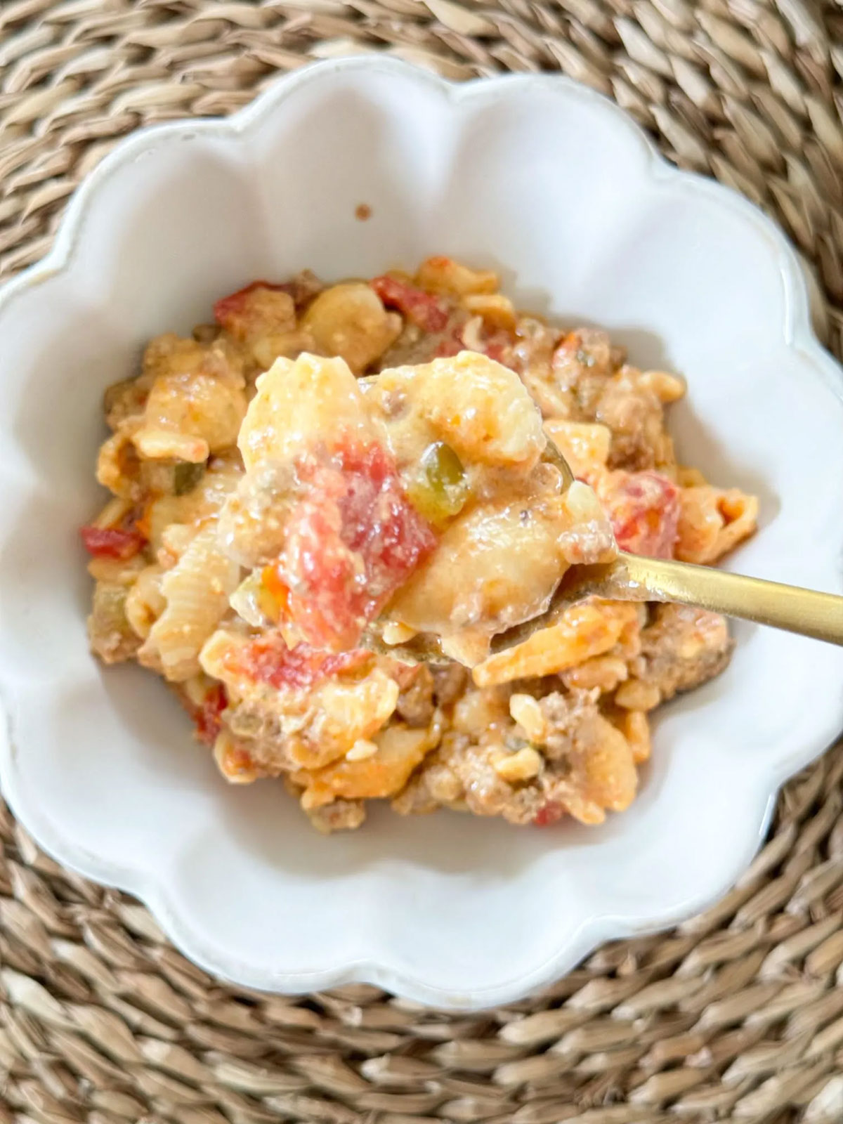 A white bowl with slow cooker cheeseburger casserole and a gold spoon holding a bite.