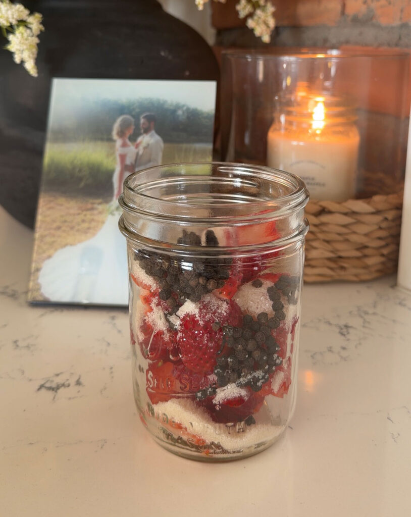 glass jar filled with strawberries, peppercorns and sugar