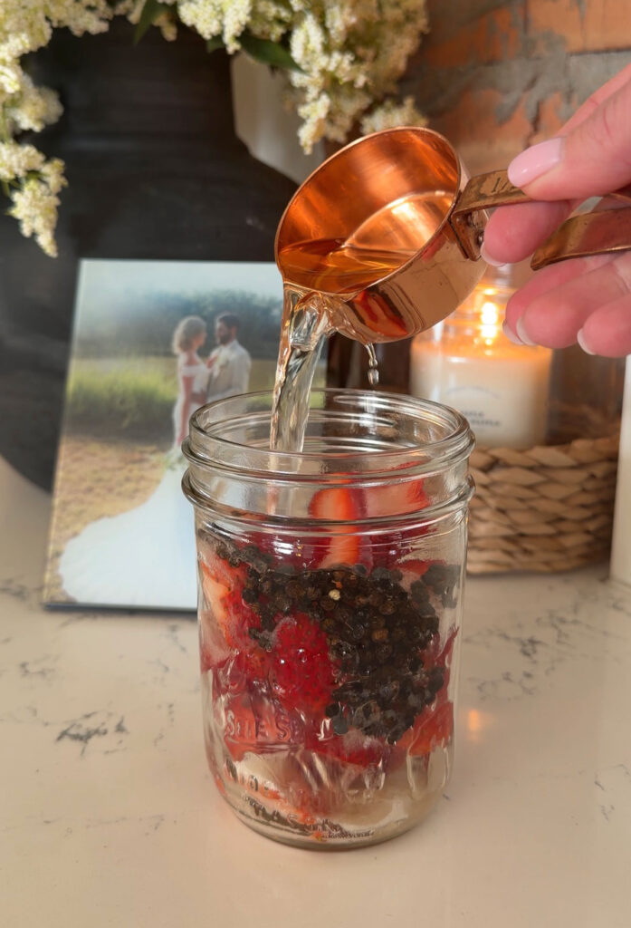 adding liquid to glass jar with strawberries and peppercorns