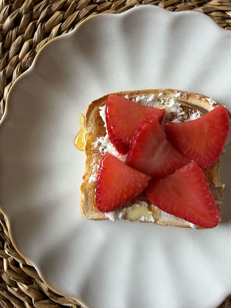 pickled strawberries sliced on toast with goat cheese and honey. white plate