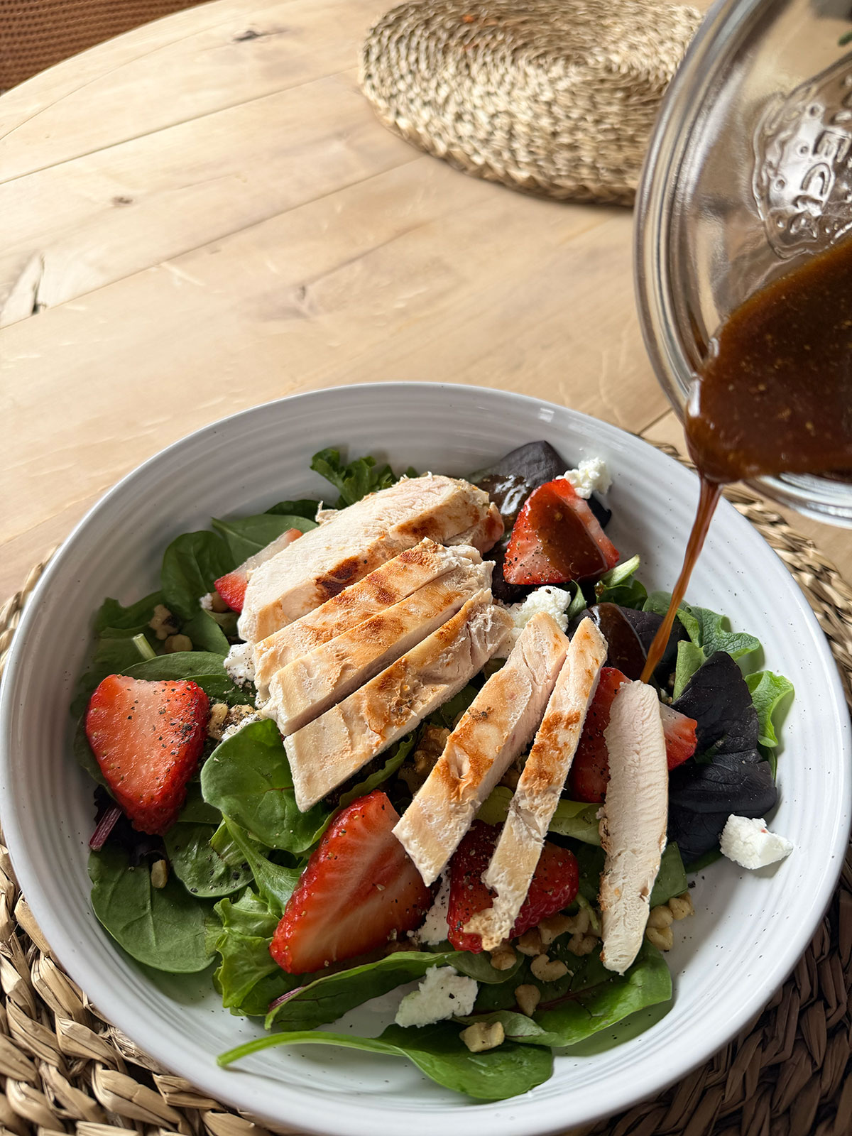 Strawberry Goat Cheese Salad in white bowl on placemat with dressing being poured over