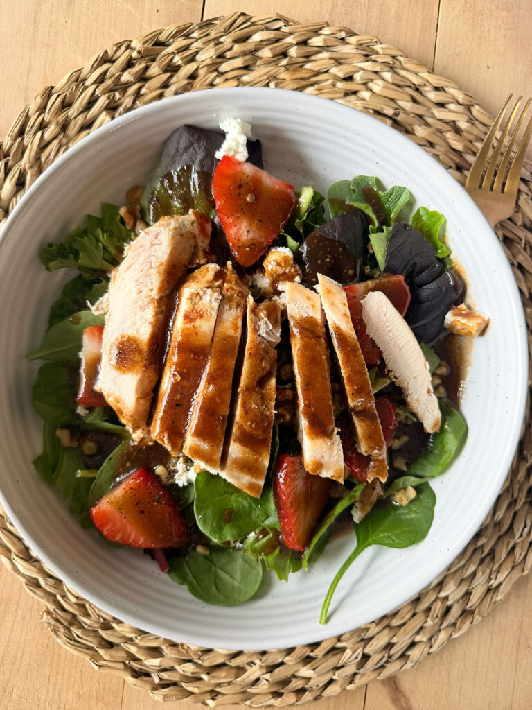 Strawberry Goat Cheese Salad in white bowl on placemat with dressing