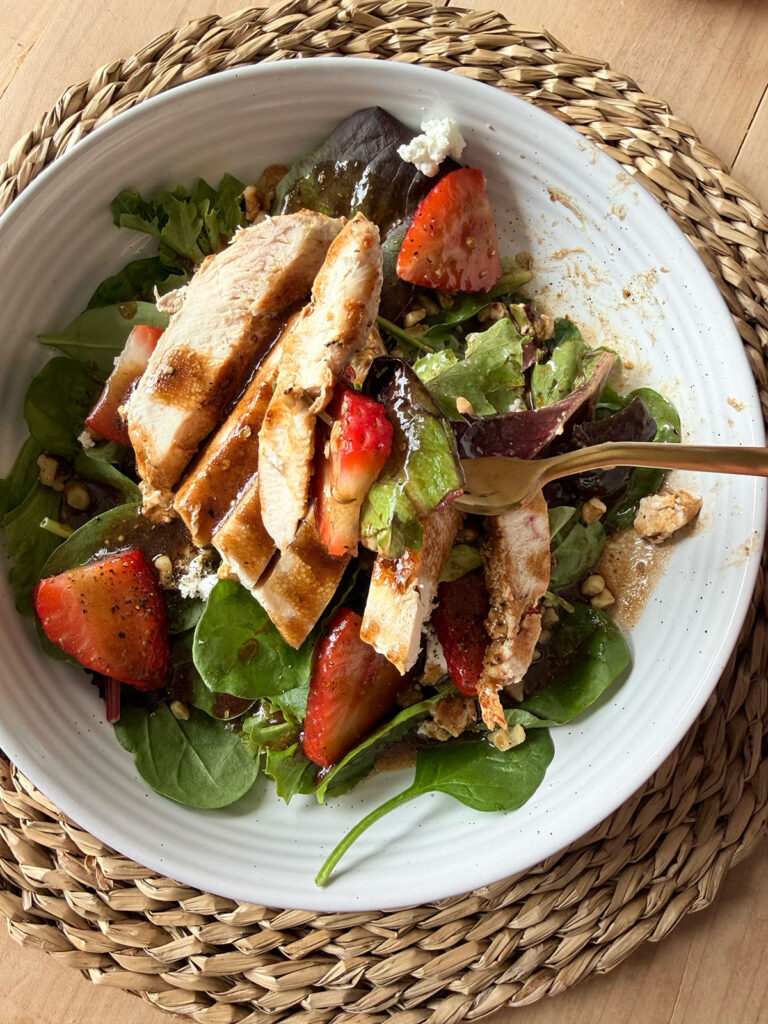 Strawberry Goat Cheese Salad in white bowl on placemat with dressing, forkful of salad