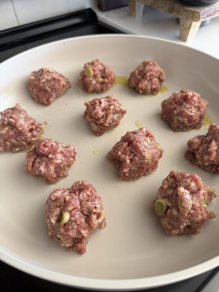pork formed into balls and in a pan with a drizzle of oil.