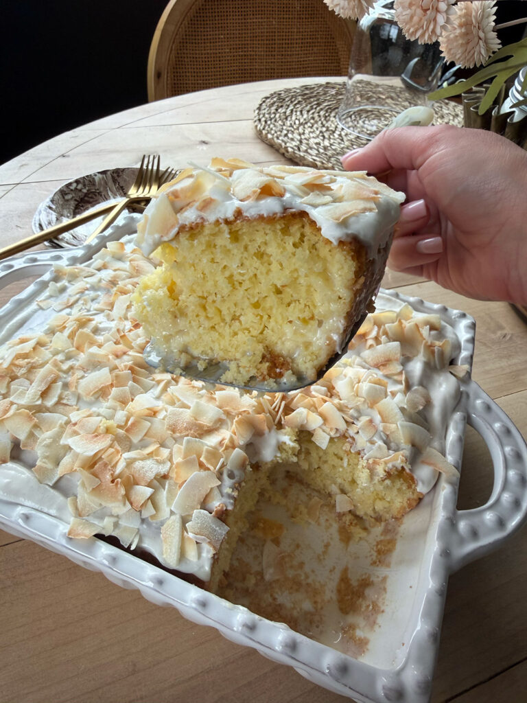 coconut poke cake in baking dish with slice of cake removed, held up with silverware and placemat in background