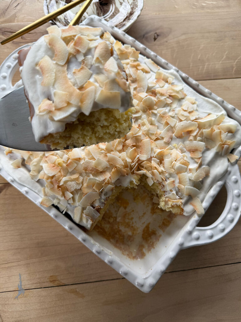 another view of slice of coconut poke cake removed from baking dish on spatula
