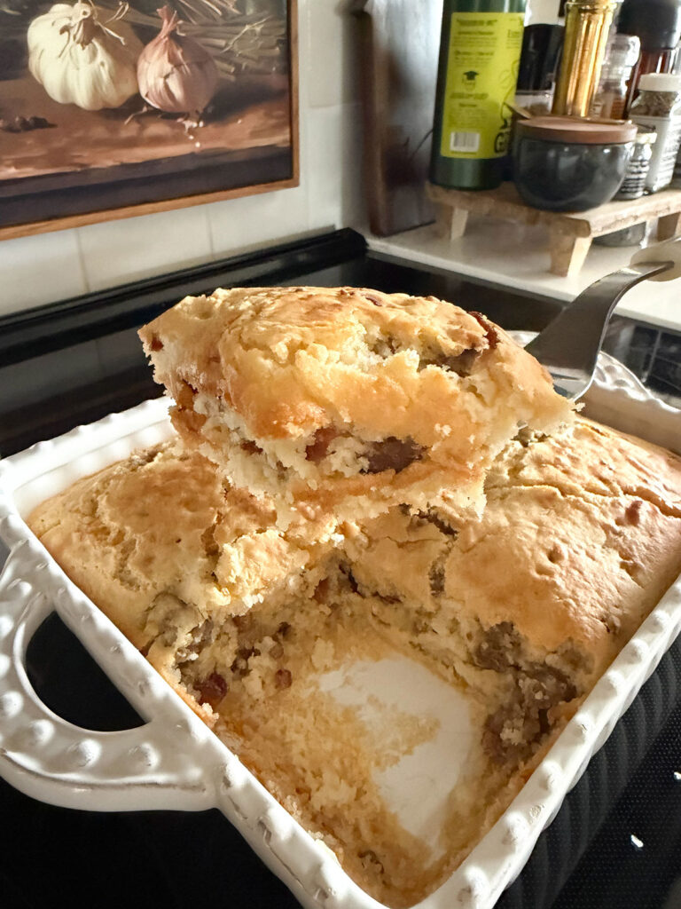 A spatula lifting out a serving of pancake sausage casserole in a white baking dish.