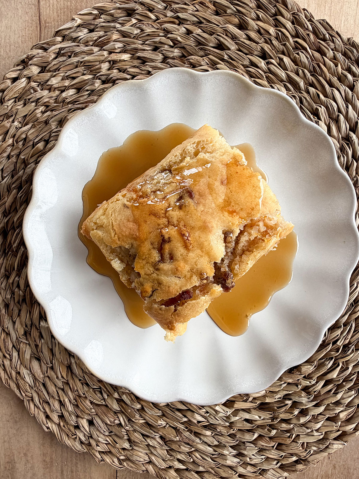 Overhead image of pancake sausage casserole with syrup on a white plate with a wicker placemat underneath.