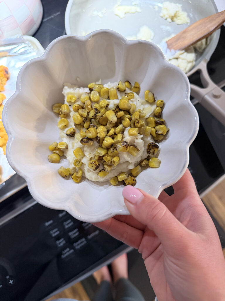 hand holding KFC bowl being built in white bowl. Potatoes and corn in bowl.