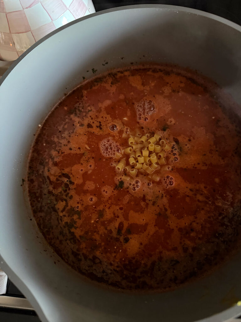 beefy tomato soup in pot with uncooked ditalini pasta added