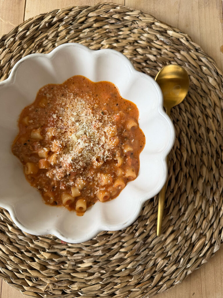 overhead view of beefy tomato soup in white scalloped bowl with gold spoon on the side of bowl, on placemat