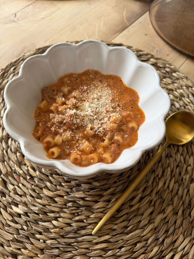 side view of beefy tomato soup in white scalloped bowl with gold spoon on the side of bowl, on placemat