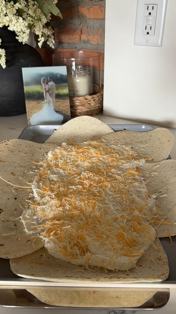 sheet pan quesadilla being built on sheet pan with meat and fillings, topped with cheese